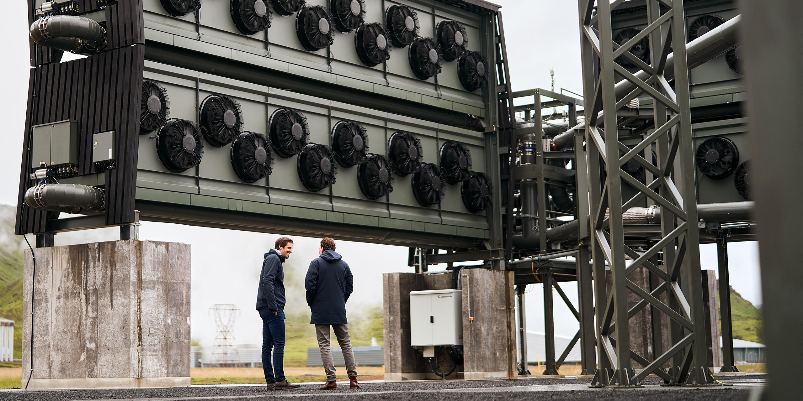 Long shot of two men underneath a large carbon-capture plant 