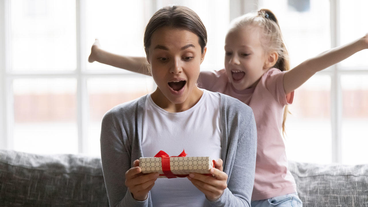 Excited daughter girl giving birthday gift box to amazed mom 