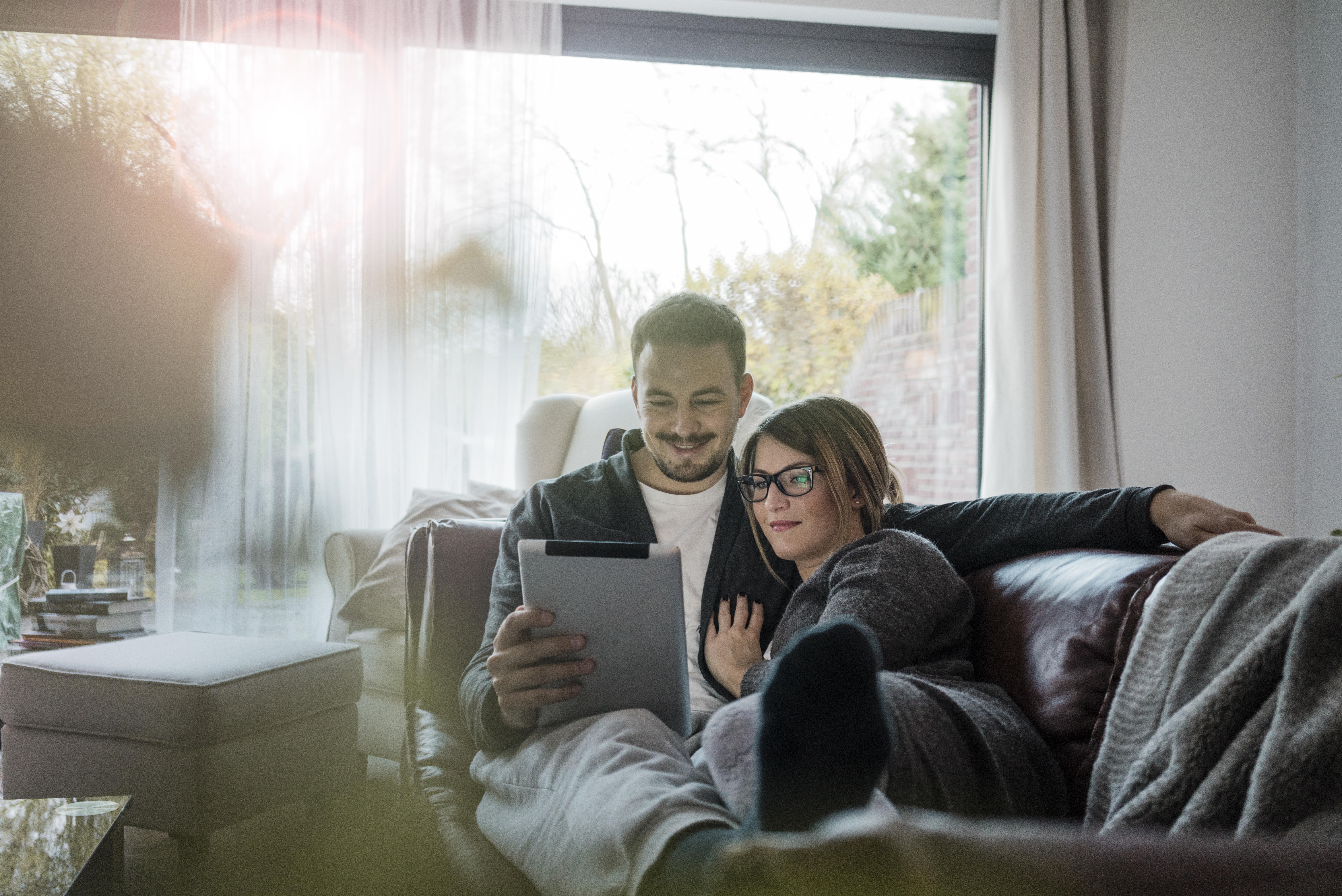 Smiling couple lying on couch at home sharing tablet 