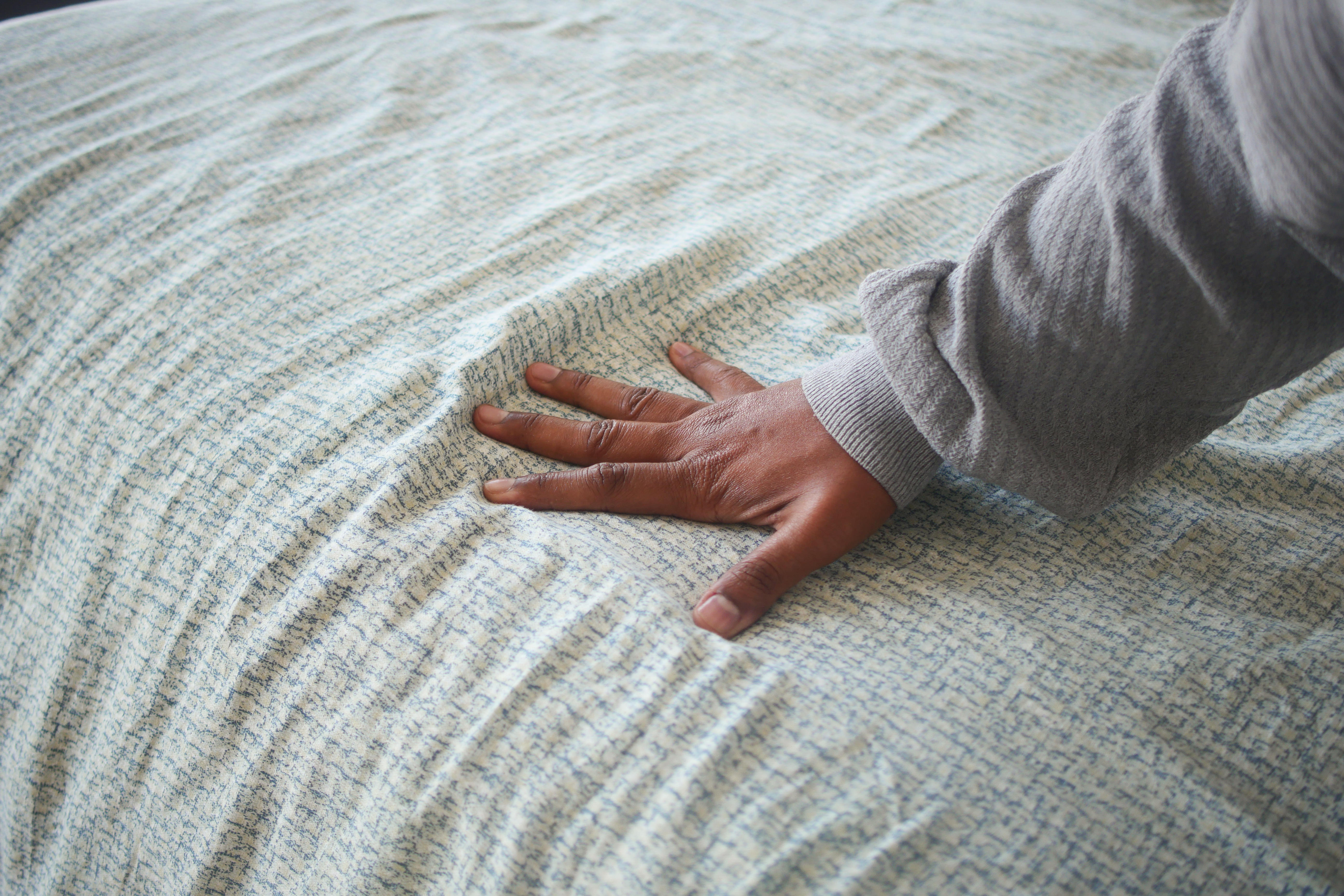 Hand touching and pressing orthopedic mattress on bed. 