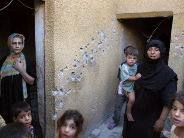 Iraqi mothers stand with their children next to a spray of bullet holes 