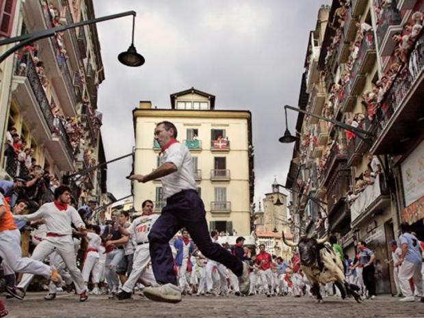 A runner is chased by a black and white fighting bull during a bullrun through the cobblestone streets of Pamplona 