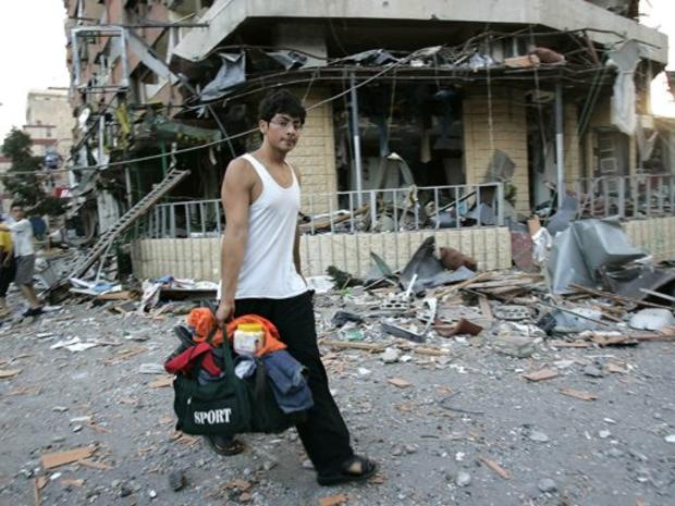 A Lebanese youth carries some belongings while walking past buildings that were damaged after Israeli air raids targeted the suburbs of Beirut, Lebanon 