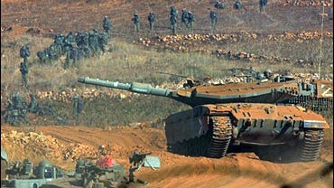 A column of Israel troops and armored vehicles approach the fence marking the border between Lebanon and Israel 