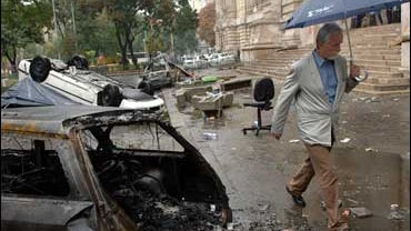 Man walks by burnt cars in front of TV building 
