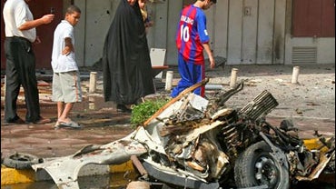 Iraqis walk past a car bomb wreck in Baghdad, Iraq 