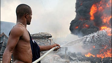 A man sprays water onto burning corpses following an early morning pipeline explosion that killed at least 200 people, in Lagos, Nigeria Tuesday, Dec. 26, 2006. 