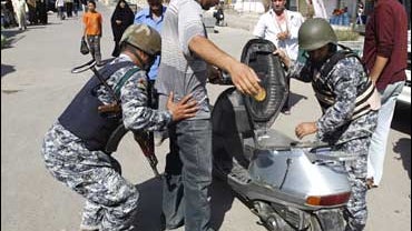 Iraqi police officers search a man in Baghdad 