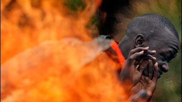 An opposition supporter shields his face from the flames of a burning makeshift roadblock in the village of Marura 