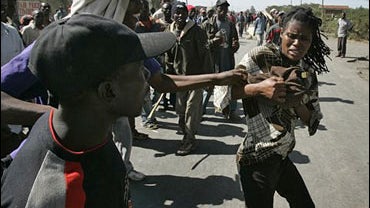 Kikuyu men cheer and push a Luo woman as she flee with all her belongings, Monday, Jan. 28, 2008 in Naivasha, Kenya. 