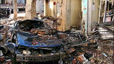 A destroyed car and damaged building are seen at the scene of a car bombing in Thenia 