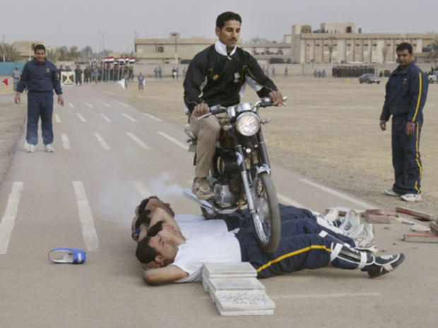 An Iraqi police graduate rides a motorcycle over his colleagues as they show their skills during a graduation ceremony 