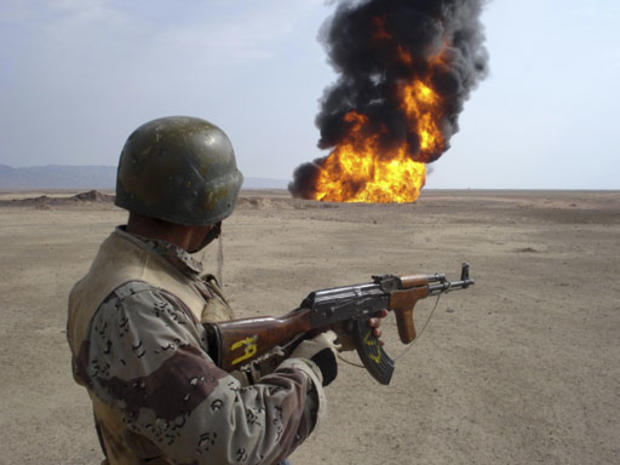 An Iraqi soldier stands guard as a pipeline burns in the background after an explosion 