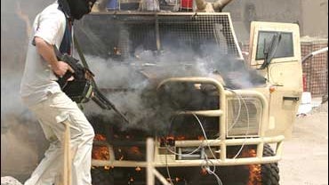 A Mahdi Army fighter stands next to a burning Iraq armored police vehicle 