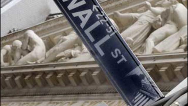 The Wall Street sign is juxtaposed against the sculpture on the facade of the New York Stock Exchange 