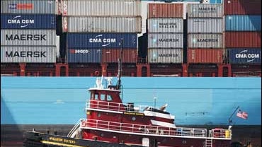 A tugboat passes a cargo ship loading and unloading containers at the Port of Newark 