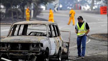 A police officer inspects a burnt out car at the township of King Lake, northeast of Melbourne 