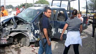 A policeman stands with others near a destroyed police vehicle after a clash with an armed group in Tepic, Mexico 