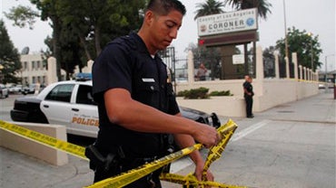 Los Angeles police officer Carlos Carrillo stretches out police tape near the entrance to the Los Angeles County Coroner's 