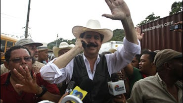 Honduras' ousted President Manuel Zelaya, waves to supporters as he speaks on a cell phone as he arrives at the Nicarugua-Honduras border in Las Manos, Nicaragua, 250 km north of Managua, Friday, July 24, 2009. Thousands of Hondurans flocked to the remote 