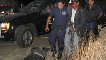 An injured bodyguard of Mexico's Michoacan state's Public Safety Security Secretary, walks helped by a police officer after being wounded during a shootout next to a fellow bodyguard who lies dead in Morelia, Mexico, early Saturday, April 24, 2010. 