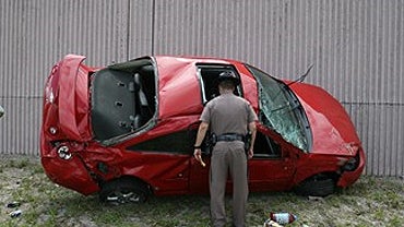 A Florida Highway Patrol officer surveys damage to the car that carried 1 1/2-year-old Jacob Mentor, who was hospitalized after being ejected from the car in an accident on I-95 in Pompano Beach, Fla., Friday, May 14, 2010. 