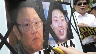 A South Korean conservative activist uses a utility knife to deface a portrait of North Korean Leader Kim Jong Il, left, and what protesters say is a portrait of his son Kim Jong Un during a rally in Seoul, South Korea, Monday, June 22, 2009.  