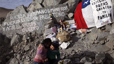 Elias Sepulveda, right, embraces her cousine Katherine next to a tribute and support site with candles, flags and messages for their relatives Esteban and Pablo Rojas, two of the 33 miners trapped at the collapsed mine San Jose in Copiapo, Chile, Monday,  
