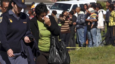 A family members react at a accident seen on the outskirts of Cape Town, South Africa, Wednesday, Aug 25, 2010. A driver taking children to school went around a closed railroad crossing gate Wednesday, then collided with an oncoming train that killed at l 
