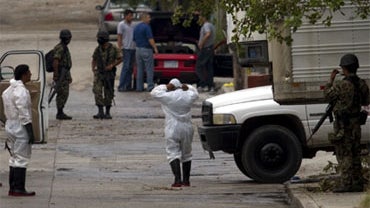 Mortuary workers wearing protective suits and Mexican marines outside a funeral home where the bodies of 72 men and women allegedly killed by the Zetas drug gang are kept in San Fernando, Mexico, Aug. 26, 2010. 