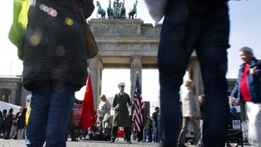 A man with an American flag and dressed as a historical U.S. soldier poses for tourists in front of the Brandenburg Gate, in Berlin on Sunday, Oct. 3, 2010. 