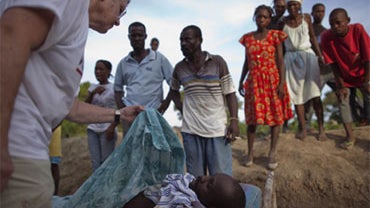 People watch a U.S. missionary doctor, who did not want to be identified, confirm the man lying in the bed died of cholera outside a hospital before being transported home in the town of Droin, Haiti, Friday Oct. 22, 2010.  