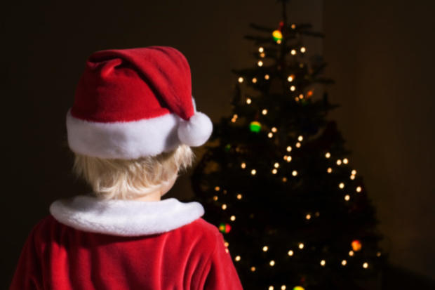 Child dressed as Santa looks at Christmas tree lights 