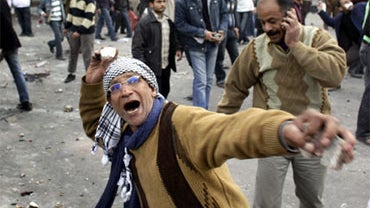 An anti-government protester throws rocks at pro-government supporters, while another talks on his mobile phone, right, during clashes between the two sides near the Egyptian Museum in downtown Cairo, Egypt, Thursday, Feb. 3, 2011. Protesters and regime s 