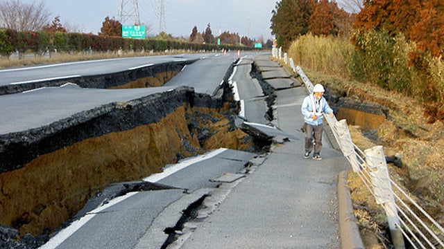 After earthquake in japan, worker examines road.  