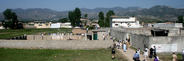 Locals and news media gather round the compound and house, seen on right, of Osama bin Laden as authorities eased  security and allowed people to approach its perimeter  