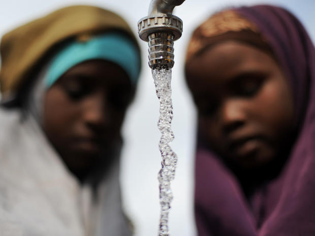 Somali girls watch water fill their jerry cans at a water distribution point 