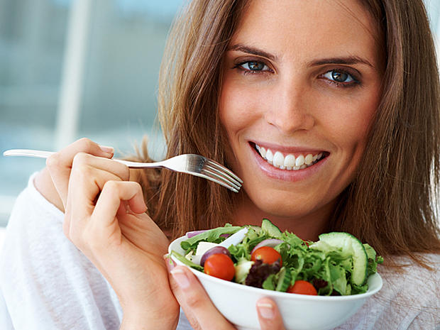Close-up portrait of happy beautiful woman eating vegetable salad 