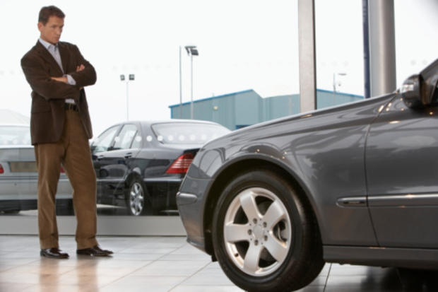 Businessman standing in front of car in showroom with arms folded 