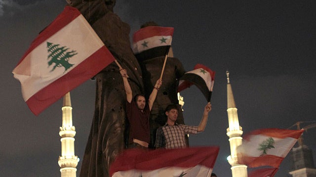 Syrian protesters stand on the Martyrs statue wave Lebanese and Syrian flags during a vigil sit-in held by Lebanese intellectuals and journalists against the Syrian regime and to show their support to the Syrian protsters who demonstrate against the Syria 