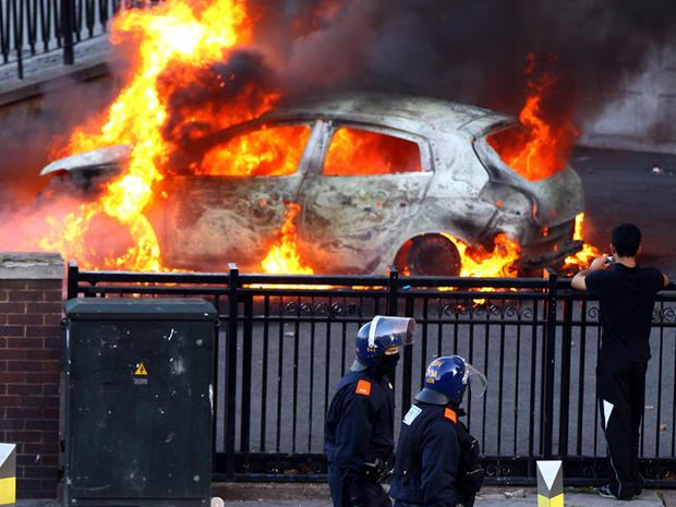Police walk past a burning car during riots in Birmingham City Centre Aug. 8, 2011, in Birmingham, England. After three nights of rioting and looting in and around London, the chaos is starting to spread to other cities around Britain. 