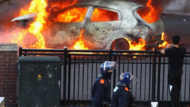 Police walk past a burning car during riots in Birmingham, England 