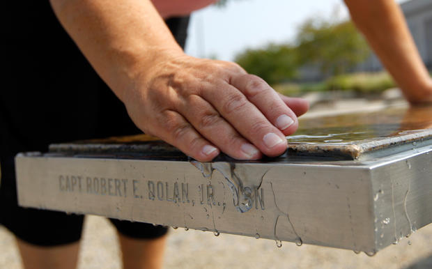 Lisa T. Dolan wipes water off the bench which bears the name of her late husband, Navy Capt. Robert E. Dolan, Jr., at the Pentagon Memorial in Arlington, Va., on Aug. 7, 2011. Capt. 