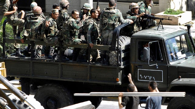 In this citizen journalism image, Syrian citizens, below right, wave to Syrian troops withdrawing from the Damascus suburb of Saqba, Syria, Aug. 14, 2011, following a campaign of raids and arrests that started overnight and continued into the morning. The 