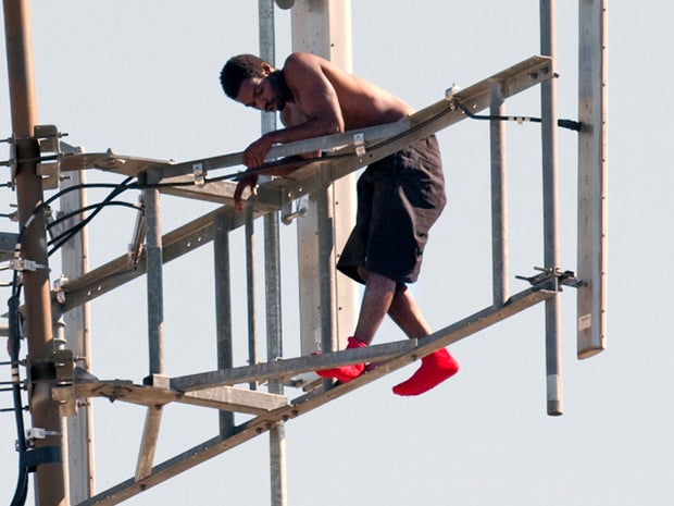 Dangling with one foot on a support beam, the man in a standoff with police rearranges himself on a communications tower Aug. 14, 2011, in Tulsa, Okla. 
