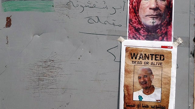 Pictures of Libya's fallen leader Muammar Qaddafi in various possible disguises with the slogan 'Wanted Dead of Alive' are plastered on a wooden road block at a checkpoint in the Tripoli suburb of Tajura on September 1, 2011 