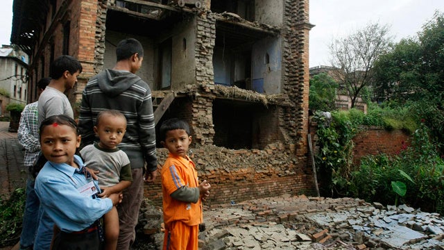 people stand near the debris of collapsed buildings 