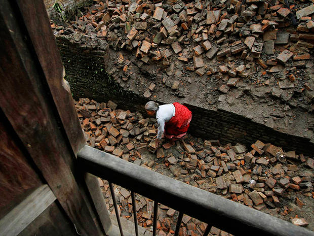 Nepalese woman removes bricks of the damaged house  