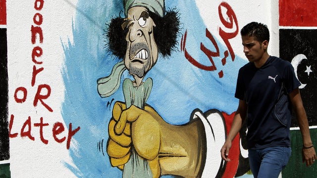 A Libyan man walks past graffiti depicting ousted Libyan leader Muammar Qaddafi in the capital city of Tripoli Sept. 27, 2011. 