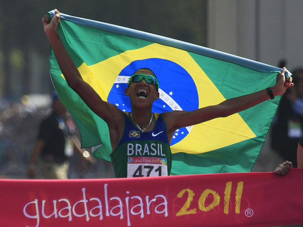 Solonei Silva holds a flag of his country as he crosses the finish 